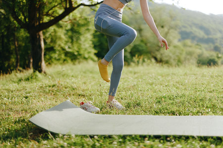 Young woman practicing yoga outdoors on a green mat, embodying health, balance, and tranquility in a...