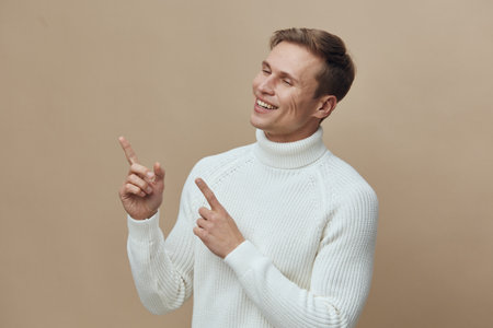 Smiling happy man in white sweater pointing upwards with both hands on beige background, casual confident expression, lifestyle concept, cheerful mood, portrait photography.の写真素材