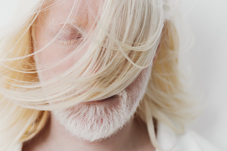 Portrait of a man with long, flowing blonde hair covering his face, set against a soft white background that enhances the serene and ethereal atmosphere of the imageの写真素材
