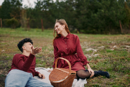 Young couple enjoying a candid picnic on a grassy field, sharing a genuine laugh and relaxed conversation, natural poses and warm tones convey authenticity and real connection.の写真素材