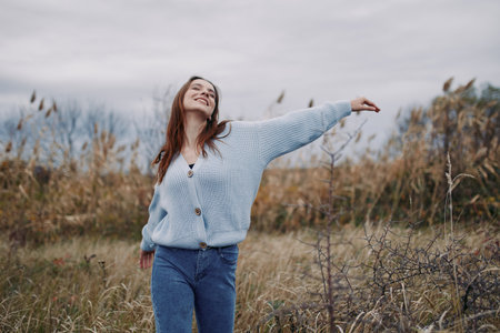 Authentic moment of a woman outdoors, wearing a knit sweater, smiling with arms outstretched, capturing genuine happiness and natural grace in an open field.の写真素材