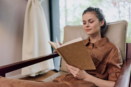 Young woman reading a book in a cozy interior, wearing casual brown attire, conveying a sense of...
