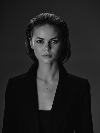 Black and white portrait of serious woman with wet hair wearing blazer in dark studio settingの写真素材