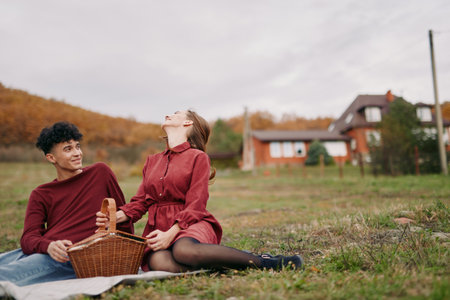 An authentic candid moment of a couple sharing a picnic in a rural field, warm tones, natural light, simple companionship, sincere smiles, quiet joy, unposed scene.の写真素材
