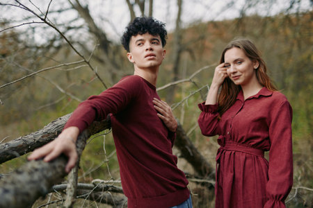 A candid pair stands in a quiet woodland, burgundy garments and relaxed pose conveying simple style...