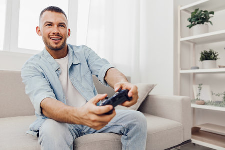Happy man playing video games in a bright living room, showcasing a modern lifestyle and the joy of...