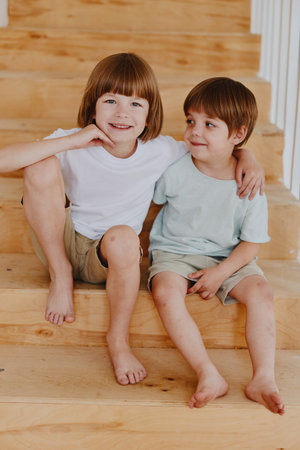 Cheerful kids sitting on wooden stairs, enjoying a moment of friendship and playfulness. Their...