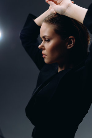 Profile of a thoughtful woman in black clothing with a dark studio background and soft lightingの写真素材