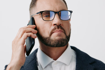 A focused business professional man on a colored isolated background speaks on a mobile phone with a confident, composed expression, exuding readiness and leadership.の写真素材