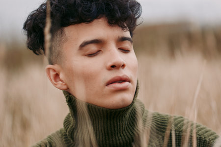Authentic portrait of a young man with eyes closed in a quiet field, calm expression, natural light, candid mood, sincere portrayal of inner peace.の写真素材