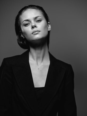 Black and white portrait of a serious woman in a dark blazer with natural makeup and slicked-back hair.の写真素材