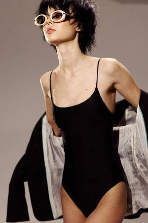 Stylish woman wearing black swimsuit and sunglasses posing confidently with jacket in studio lighting.の写真素材