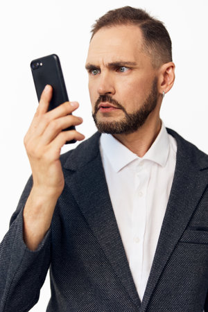 Professional man in a blazer studies a mobile device, conveying focus and determination. Solid color background highlights a confident, thoughtful business persona.の写真素材