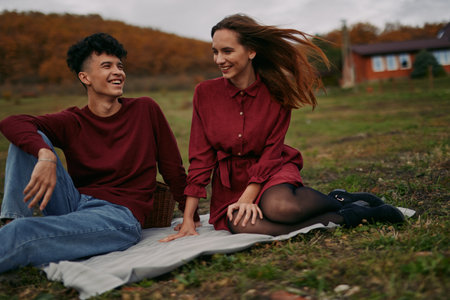 A candid scene captures authenticity and credibility as friends laugh and relax on a picnic blanket, enjoying a cool autumn breeze under a mellow sky with warm tones.の写真素材