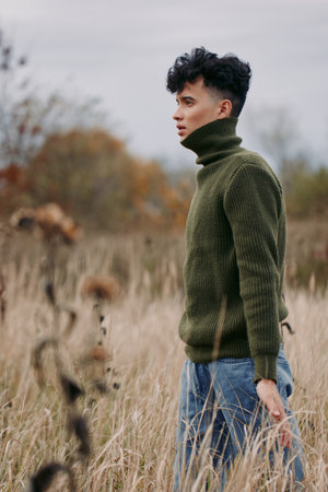 A candid portrait of a lone model standing in tall grass, wearing a forest green knit turtleneck, conveying authenticity and quiet realism in natural light.の写真素材