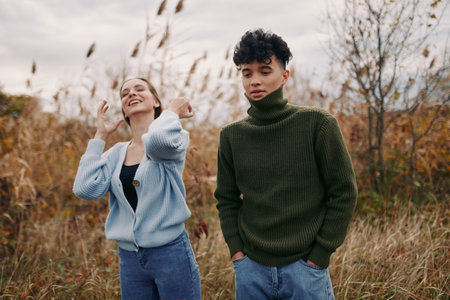 Two young adults stand in a windswept autumn field, captured in a candid, authentic moment that highlights genuine emotion, natural interaction and visual credibility and quiet atmosphere.の写真素材