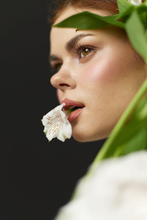 Young woman with natural makeup, holding a white flower, radiating serenity and elegance against a dark green backdrop, embodying beauty and tranquilityの写真素材