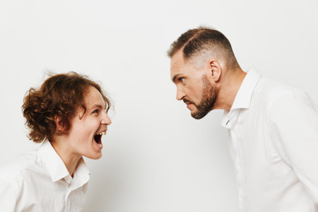 A business professional man stands against an isolated colored backdrop, displaying intense emotion as he faces a colleague in a tense, high energy moment of confrontation.の写真素材