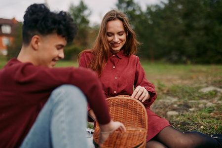 A young couple shares a relaxed outdoor picnic moment, candid smiles and gentle interaction capturing authenticity and credibility in a natural, unstaged scene focused on genuine connection.の写真素材