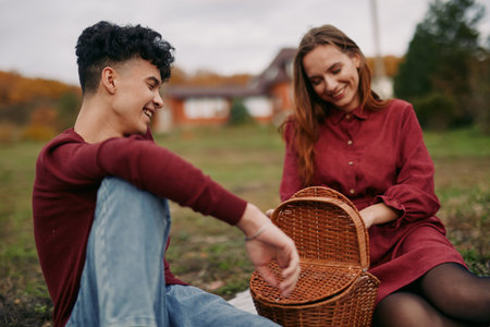 Two friends share an authentic moment outdoors, sitting on grass with a woven basket, honest smiles, and relaxed posture, conveying truth through simple connection.の写真素材