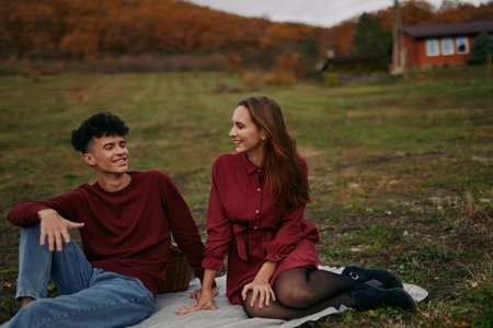A relaxed young couple shares a candid outdoor moment on a blanket in an autumn meadow, conveying genuine connection and subtle authenticity through natural expressions.の写真素材