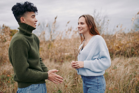 An authentic candid moment between two people sharing a conversation in a natural field, capturing genuine interaction, warmth, and realism in soft daylight.の写真素材