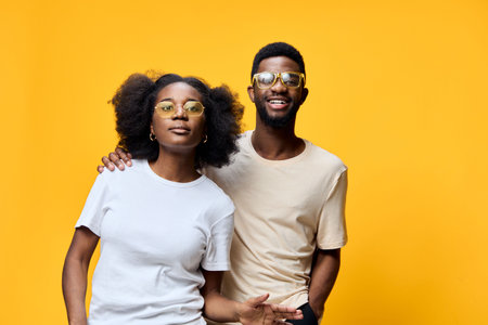 Young African models wearing trendy sunglasses, posing joyfully against a vibrant yellow background, expressing happiness and confidence in casual summer attireの写真素材