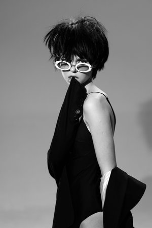 Stylish woman with short black hair wearing white sunglasses and black outfit in black and white portrait.の写真素材