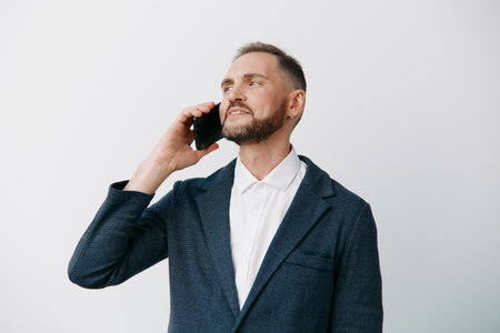 A professional businessman on an isolated colored background, talking on a mobile phone. He shows confident focus and calm determination, signaling leadership and clear communication.の写真素材