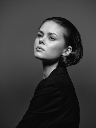 Black and white portrait of a pensive woman with short hair wearing a dark outfit in studio lighting.の写真素材