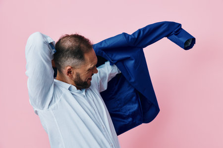 Professional man in a pastel pink studio setting, removing his blazer as he prepares for work, projecting calm confidence and focus in a vibrant color backdrop.の写真素材