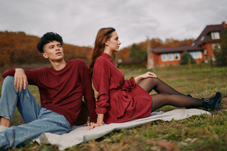 A young couple sits on a blanket in a rural autumn field, sharing a quiet, genuine moment of connection and contemplation that emphasizes natural emotion and visual authenticity.の写真素材