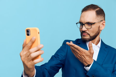 A business professional man on a vibrant blue background taking a selfie with a smartphone, displaying thoughtful, focused emotions and confident posture.の写真素材
