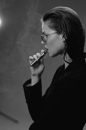 Woman vaping with glasses in black and white, profile view with smoke, stylish and modern concept.の写真素材