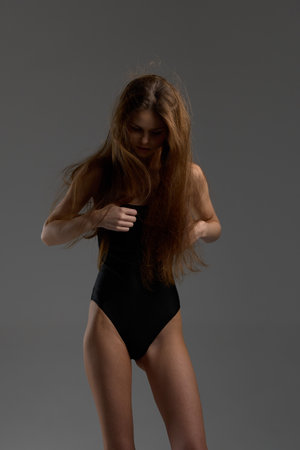 Young woman in black swimsuit with long hair posing on gray background, soft lighting, thoughtful moodの写真素材