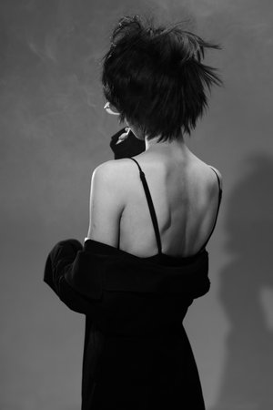 Black and white portrait of a woman with short hair and bare back wearing a strap dress and coat, artistic and moody atmosphere.の写真素材