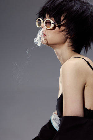 Young Asian woman wearing round sunglasses smoking with gray background and modern style.の写真素材