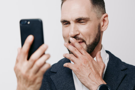 A professional man in a dark blazer checks his smartphone, depicting a focused business moment. He pauses with a thoughtful gesture, set against an isolated colored background.の写真素材