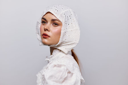 Young woman in a white bonnet and blouse, showcasing serene emotions against a light gray background, emphasizing vintage beauty and delicate styleの写真素材
