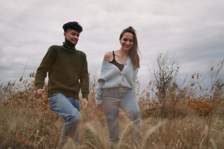 A candid outdoor image of a young couple walking through tall grass on an overcast day, capturing...