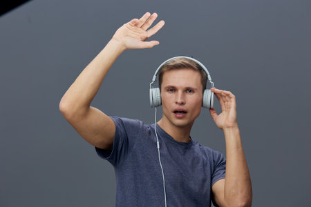 Young man with headphones listening to music on gray background, raising hand and singing with expression, casual clothing, studio portrait, people lifestyle concept.の写真素材