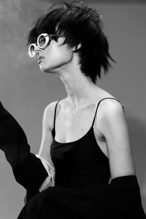Black and white portrait of a stylish woman with short hair wearing sunglasses and a black dress in...