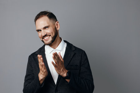 A confident businessman on an isolated gray background, dressed in a dark blazer and white shirt, exudes friendly energy and positive professional emotion.の写真素材