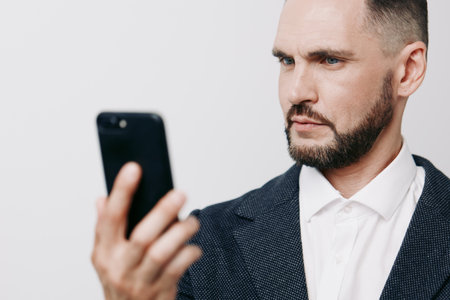 A focused business professional man checks his smartphone, signaling confidence, concentration, and modern focus against an isolated colored background with crisp lighting.の写真素材