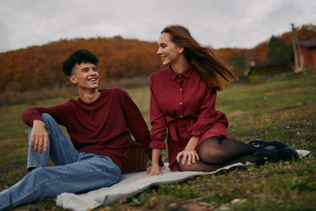A candid scene captures two people sitting on a blanket in an autumn meadow, conveying authenticity and realism through relaxed pose and genuine smiles.の写真素材