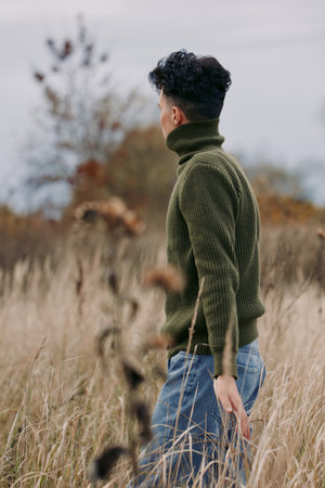 An authentic, candid portrait of a man seen from behind as he walks through a tall grass field in a...