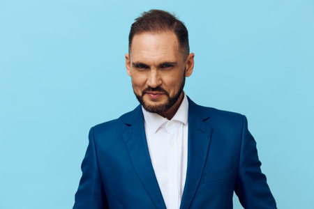 A professional man stands against a solid blue background, a clean studio portrait conveying business poise, focused presence, and ready leadership in a corporate setting.の写真素材