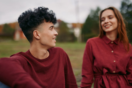 A candid portrait of a young couple sharing a genuine moment outdoors, capturing natural expressions and authentic connection with relaxed posture and soft seasonal background.の写真素材