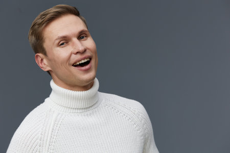 smiling young caucasian man wear white knitted sweater look camera cheerful happy isolated gray background mental health and gadgets conceptの写真素材