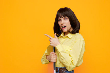 Vibrant studio portrait featuring a young woman in a bright yellow shirt, pointing playfully while posing with a prop against a bold orange backdrop, suitable for lifestyle and advertising campaigns.の写真素材